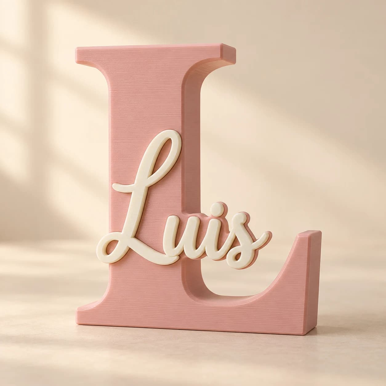 Imagen generada con IA de una inicial L rosa pastel con el nombre Luis en cursiva color crema al frente. Es una referencia ilustrativa, no un producto fotografiado.